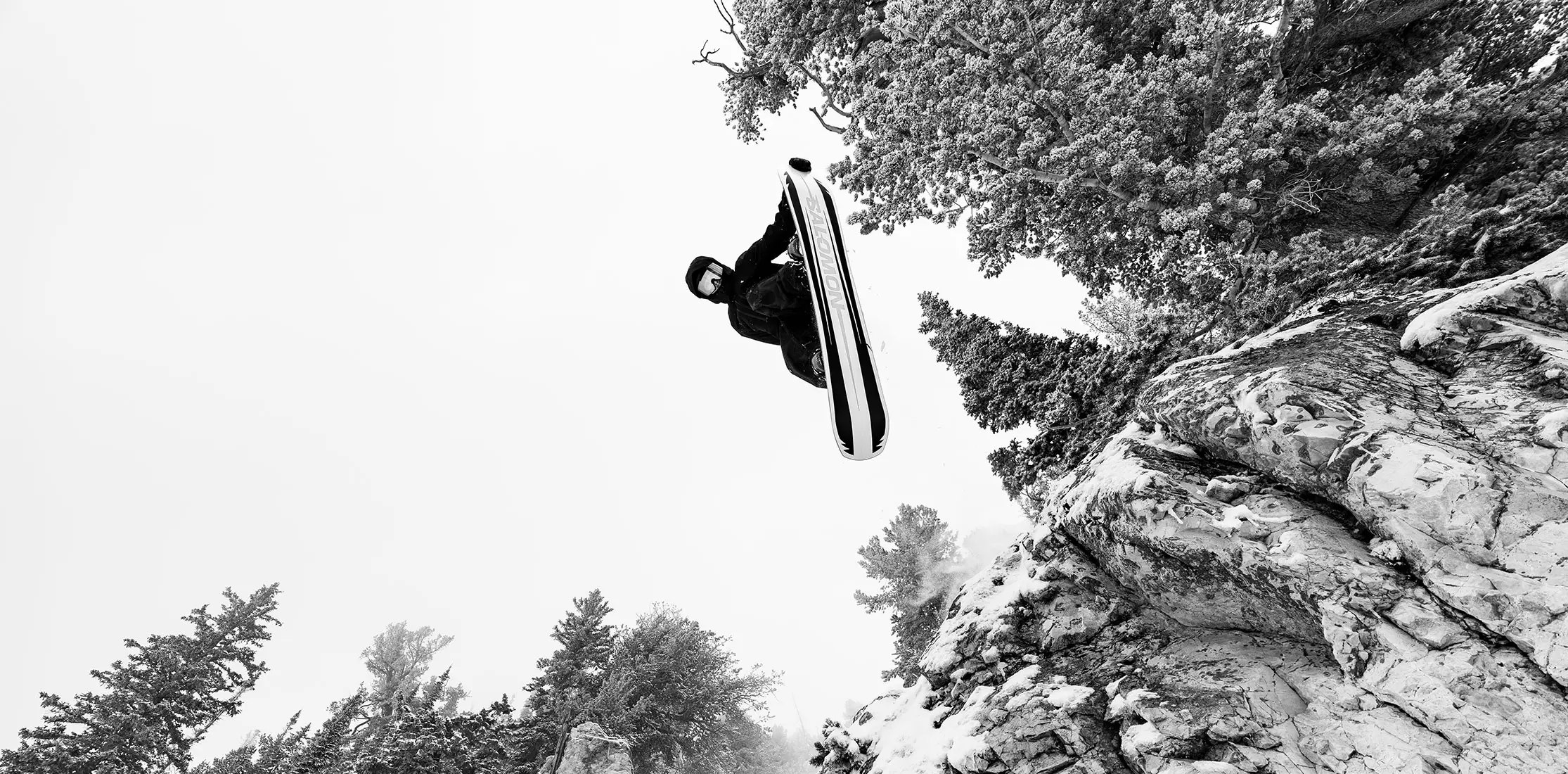 Snowboarder in black and white jumping off a cliff