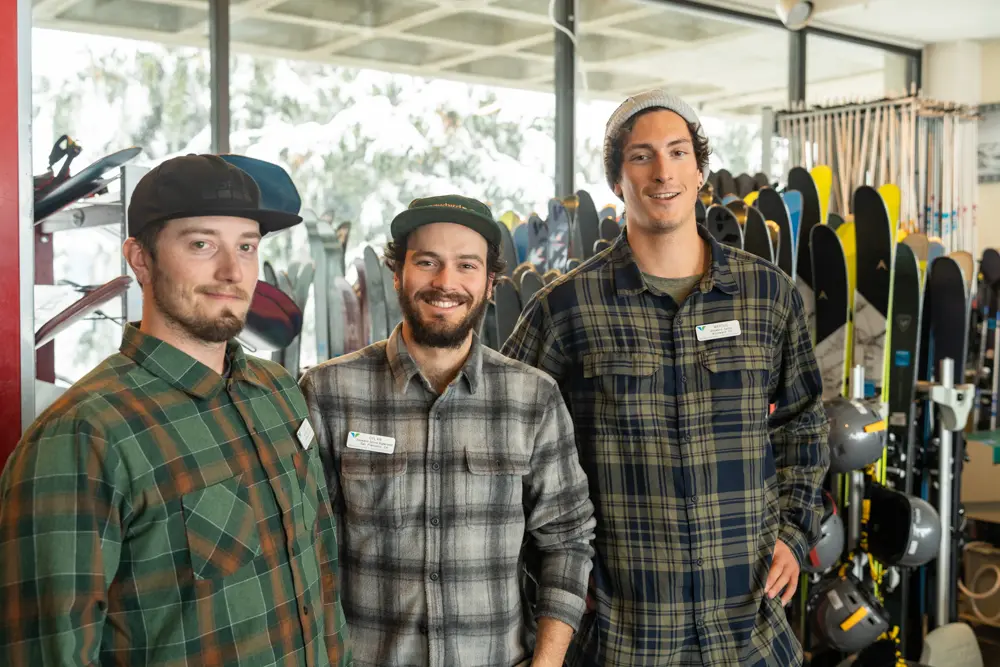 Rental shop employees smiling infront of the rental and demo gear at Snowbird's rental shops