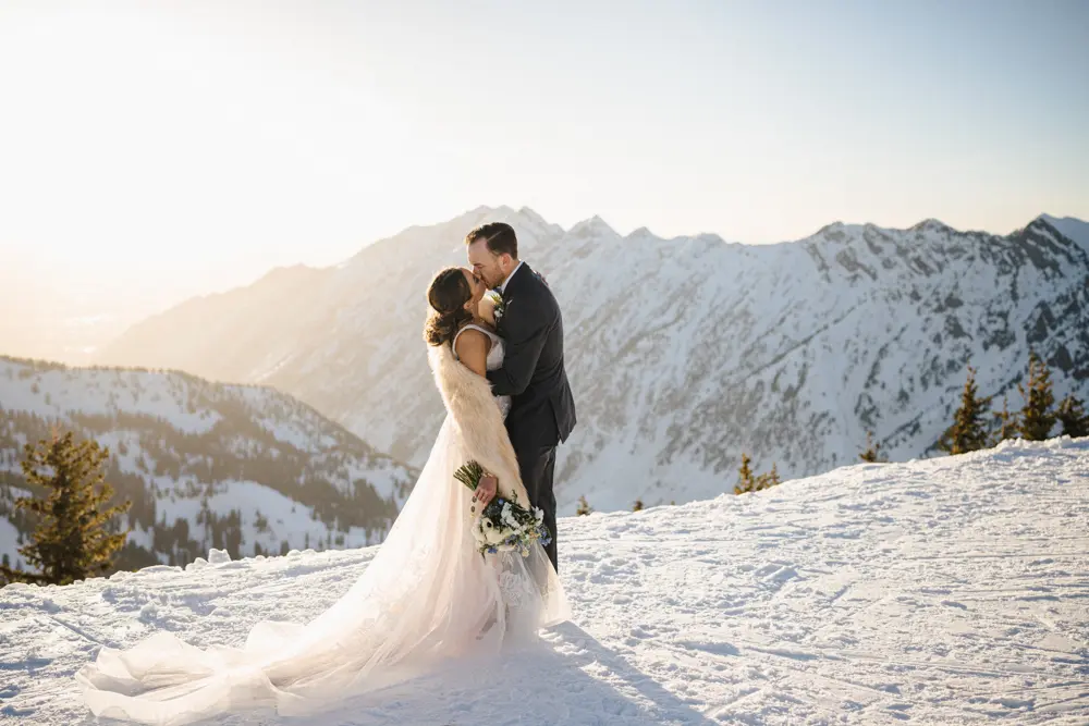 Bride and Groom kiss at Hidden Peak with a sunset canyon view in winter behind them