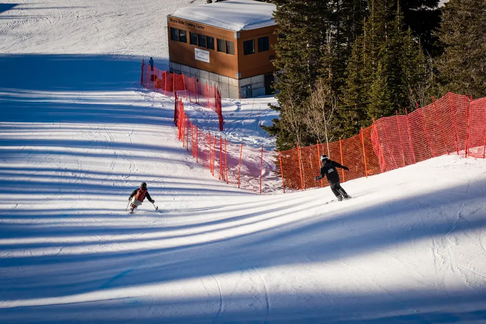 Sit skier skis down infront of Wasatch Adaptive Sports volunteer