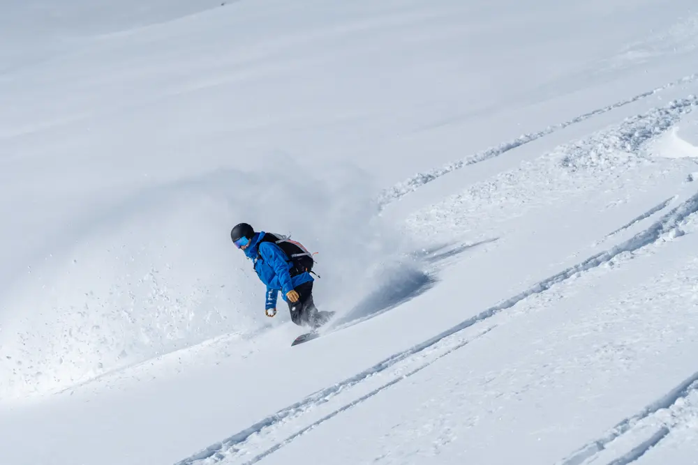 Employee with blue coat snowboards in untouched powder at Snowbird