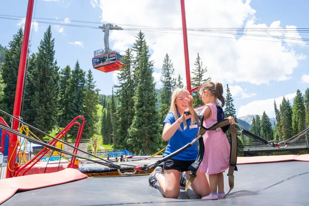 Snowbird Employee helps a girl on the bungee trampoline get buckled in