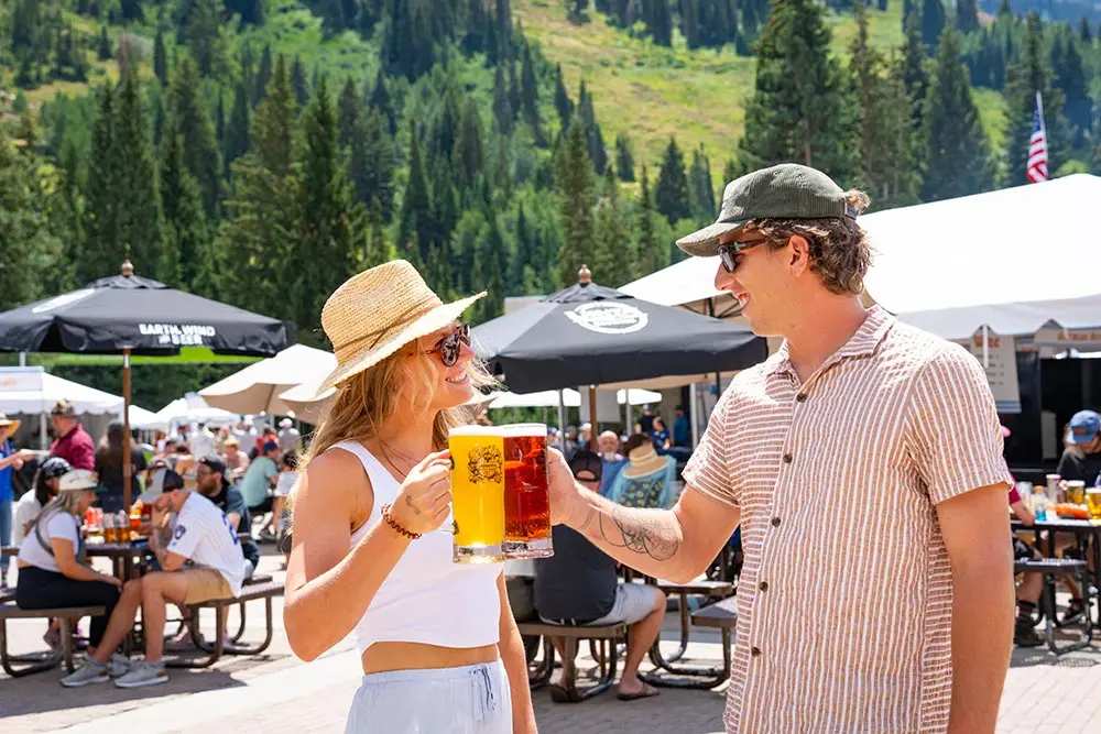 2 friends cheersing beer at Snowbird's Oktoberfest, outside in the sun
