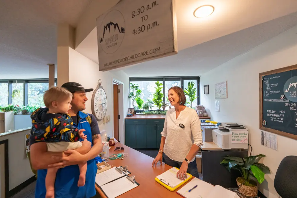 Parent in a Snowbird blue vest checks in their kid to Superior Childcare
