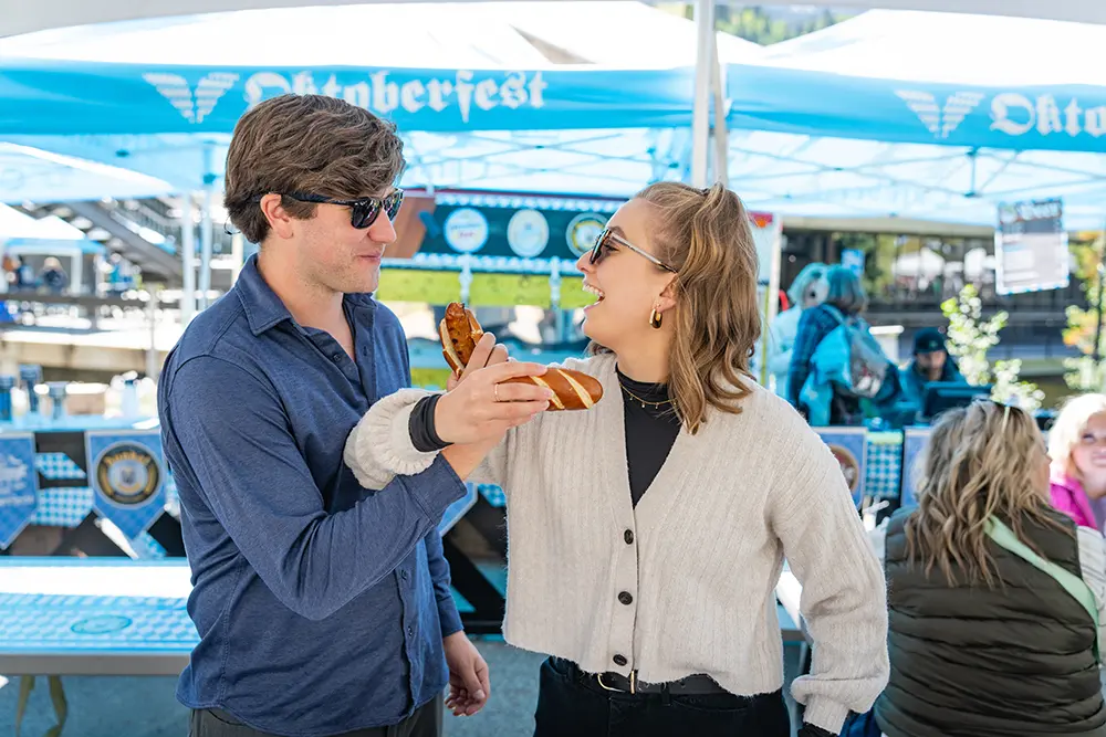Couple at Snowbird's Oktoberfest link arms and eat bratwursts