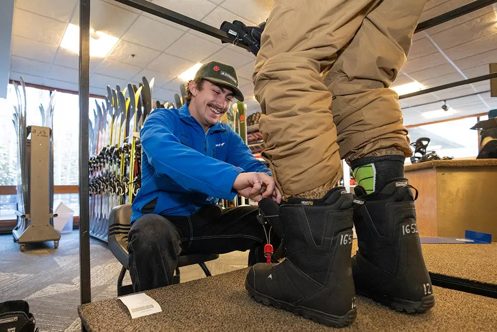 Snowbird employee helps fit Snowboard boots for a customer at a retail shop