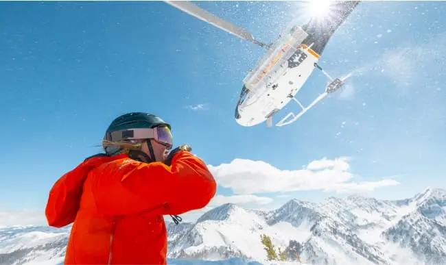 skiier with a helicopter flying overhead in front of them