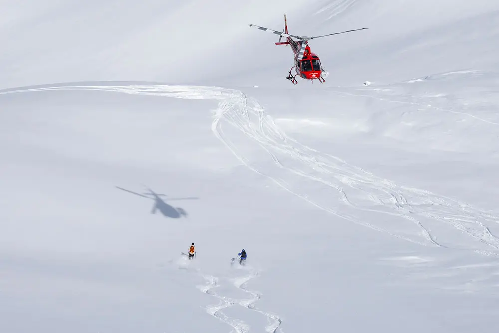 Helicopter hovers over two skiers in powder