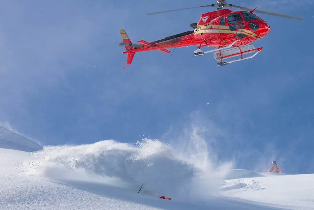 Person in cloud of powder beneath a powderbird helicopter