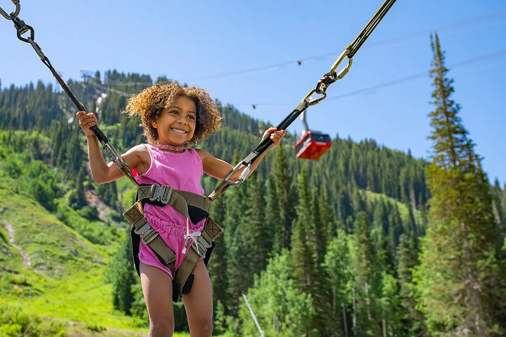 Girl jumps on the bungee trampoline at Snowbird with the tram in the back, all-day activity passes are part of Snowbird & Save