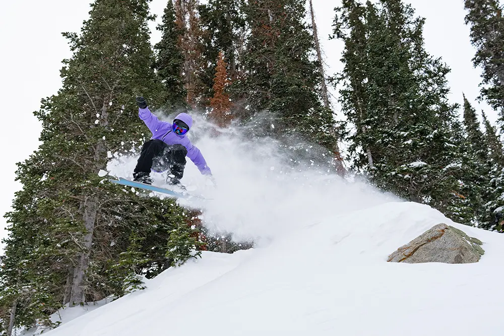 Kid on the all-mountain team at snowbird launches off a rock on a snowboard.