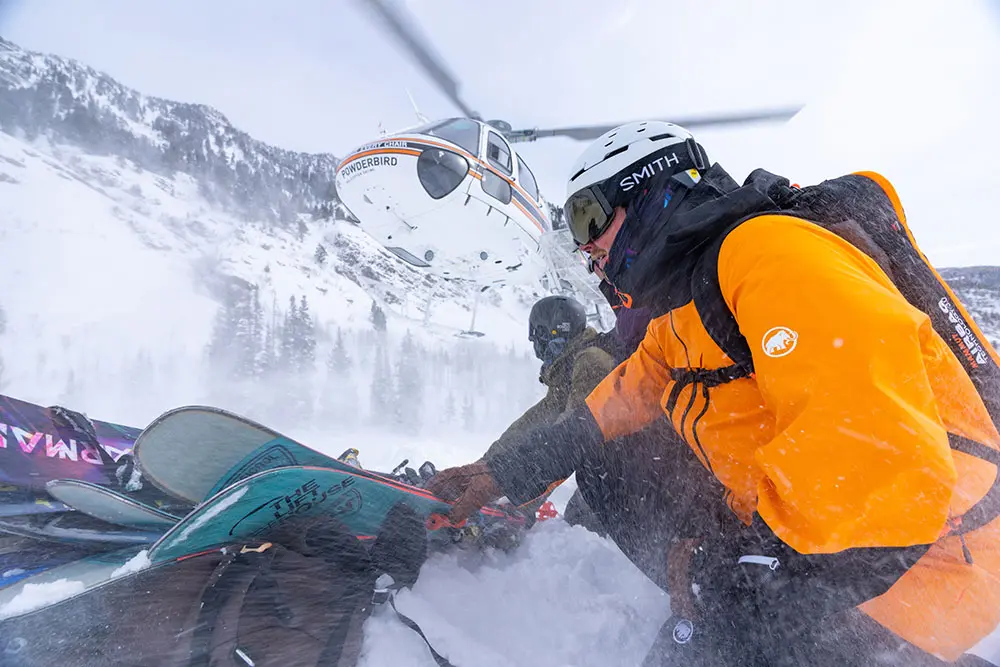 Semi-Private helicopter group crouched down as the helicopter lands near their skis