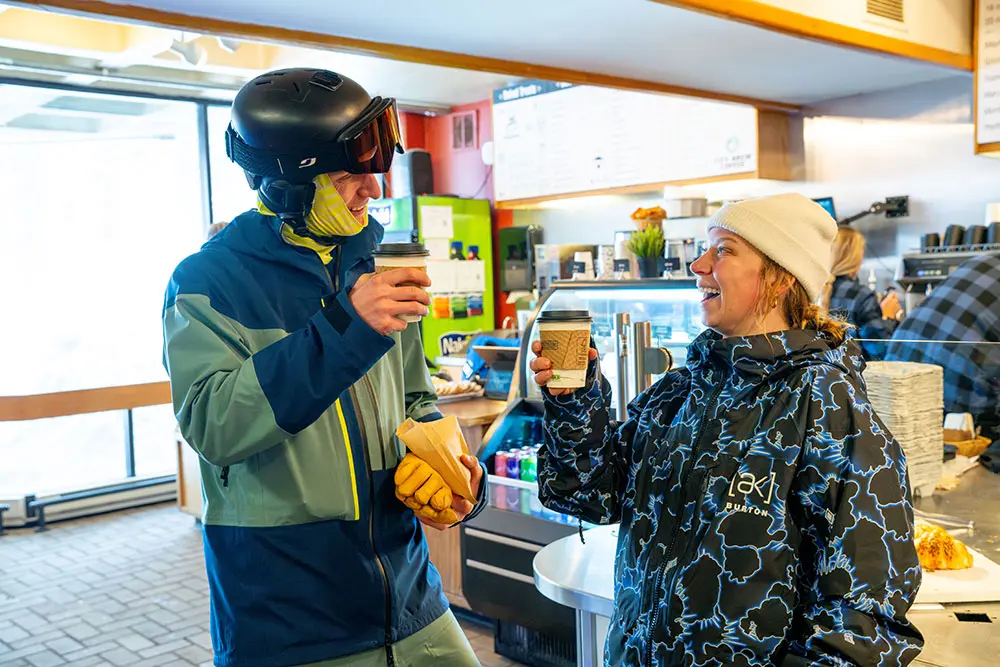 Friends laugh and cheers with paper coffee cups at Snowbird's baked and brewed cafe