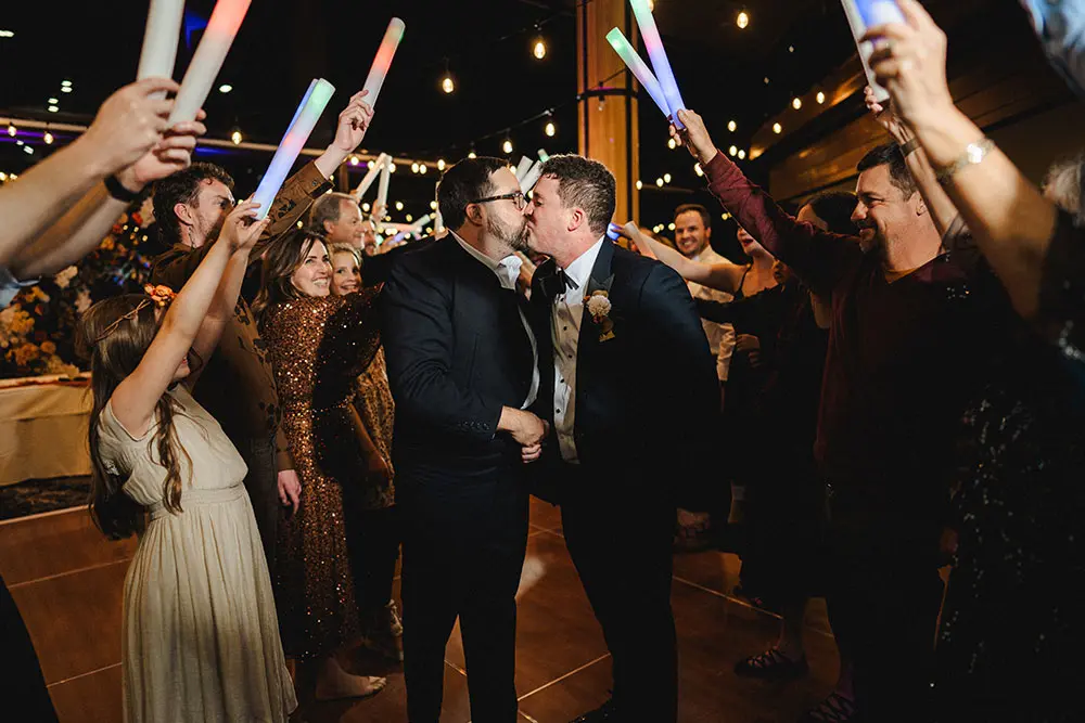 Couple kisses under their friends holding up light sticks at a Snowbird Wedding