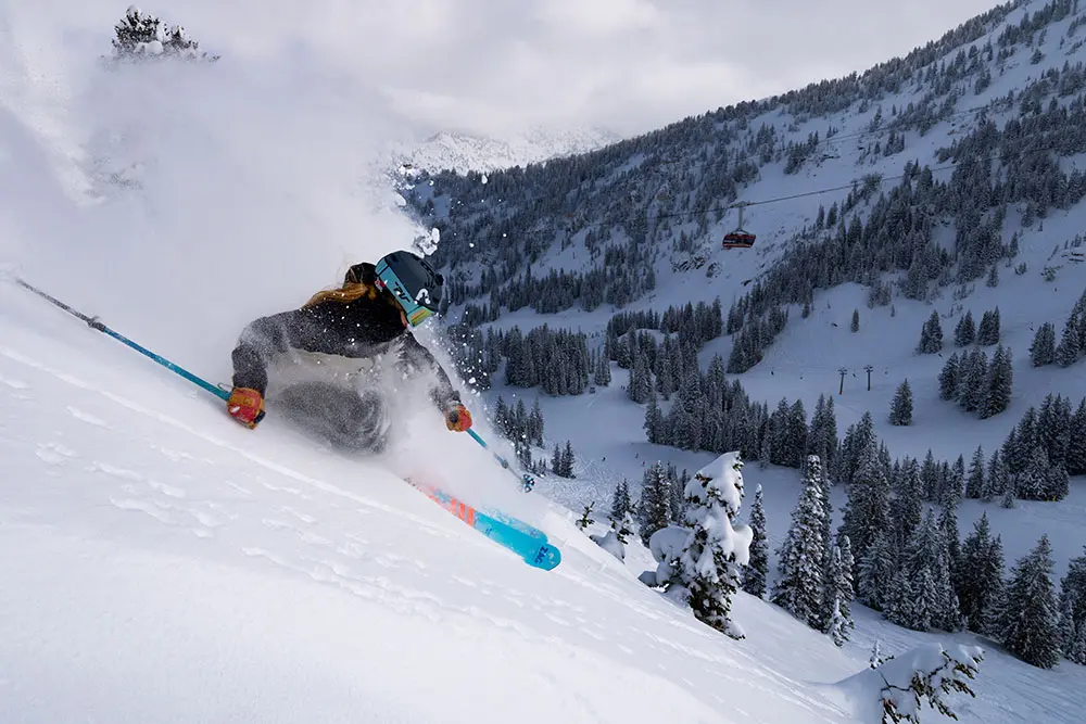 Skier in powder with the red tram behind her making a slash at Snowbird. Snowbird offers the best skiing and snowboarding in Utah