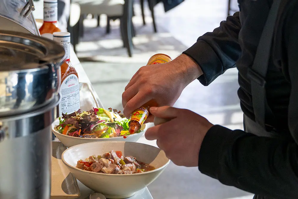 Person adds hot sauce to a bowl of soup at Powderbird