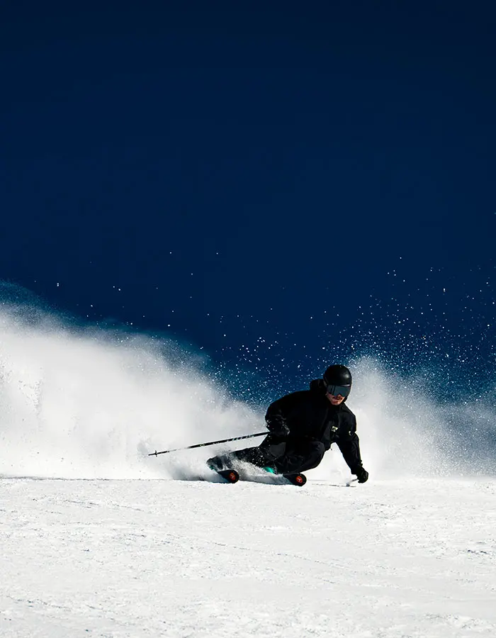 mobile hero- skier on groomer with cloud of snow behind him on a bluebird day