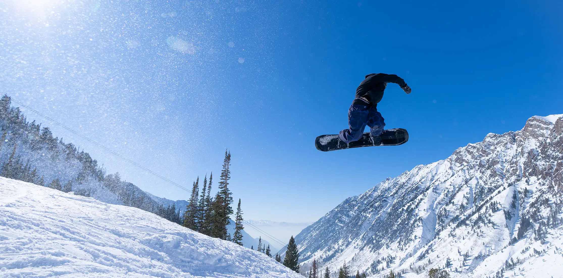 Snowboarder on a bluebird day hitting a jump during Snowbird's Spring lodging sale