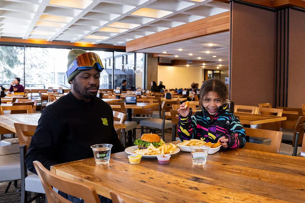 Dad and daughter enjoy a lunch at the Rendezvous, featuring a burger, chicken nuggets and fries. The rendezvous is Snowbirds self-service lunch restaurant
