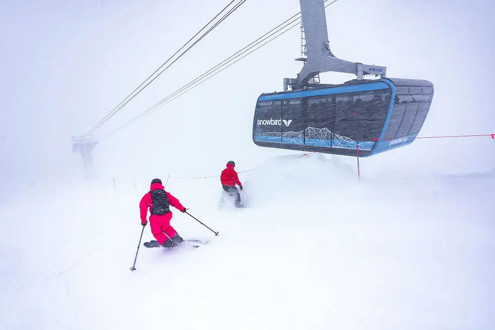 2 skiers next to the Tram at Snowbird during a storm