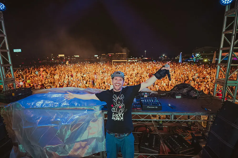 DJ stands on a stage with a crowd behind him