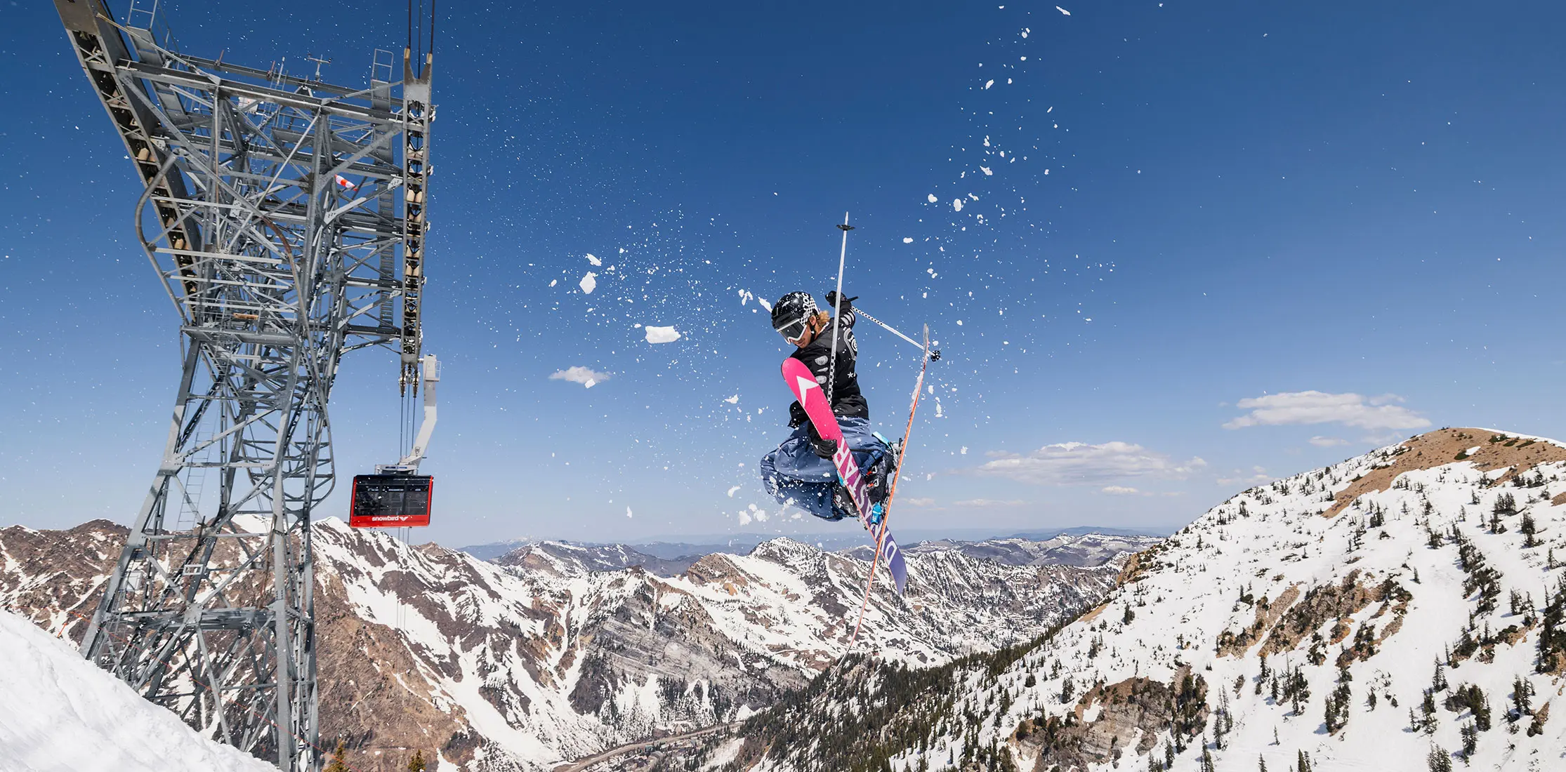 Skier hits a jump at Snowbird above Mt Baldy with the Tram rising next to him. Spring conditions