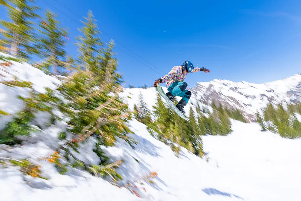 Snowboarder jumps off cliff in a party shirt during spring at Snowbird