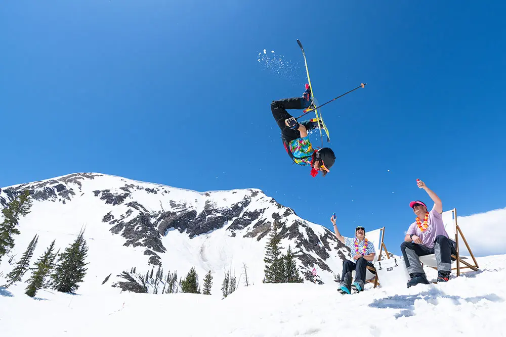 Skier flips over 2 people sitting in fold out chairs, everyone is in a party shirt