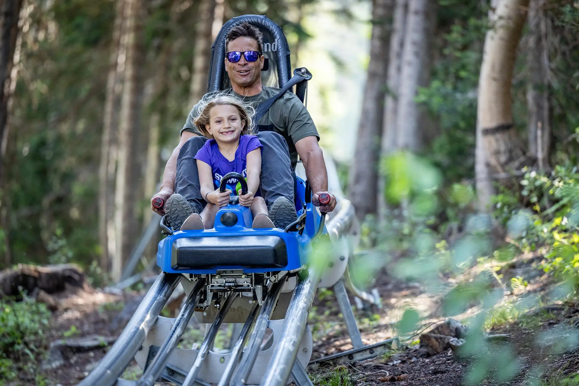 Girl and dad ride the Mountain Coaster at Snowbird in the trees