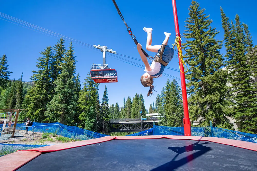 Kid flipping on the trampoline with the Summer tram rising behind her