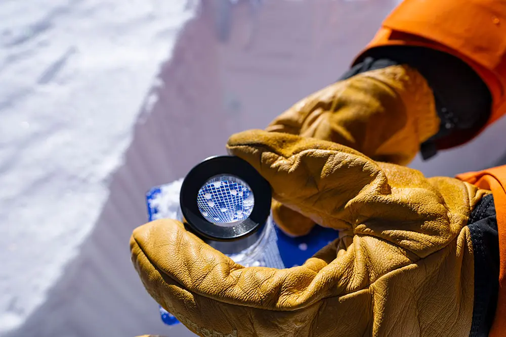 Guide with Snowbird Mountain Guide looks closer at snow under a field magnifier during an AIARE 2 course
