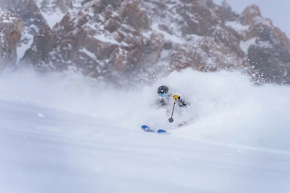 Skier who is part of the Big Mountain Camp skis by the cliffs at Snowbird