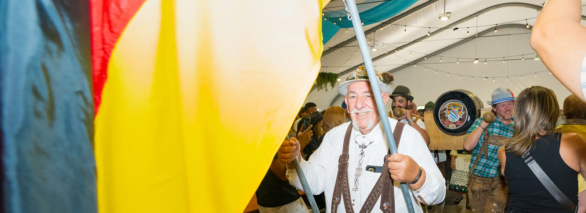 An oktoberfest flag bearer walks in with a german flag, followed by the official keg