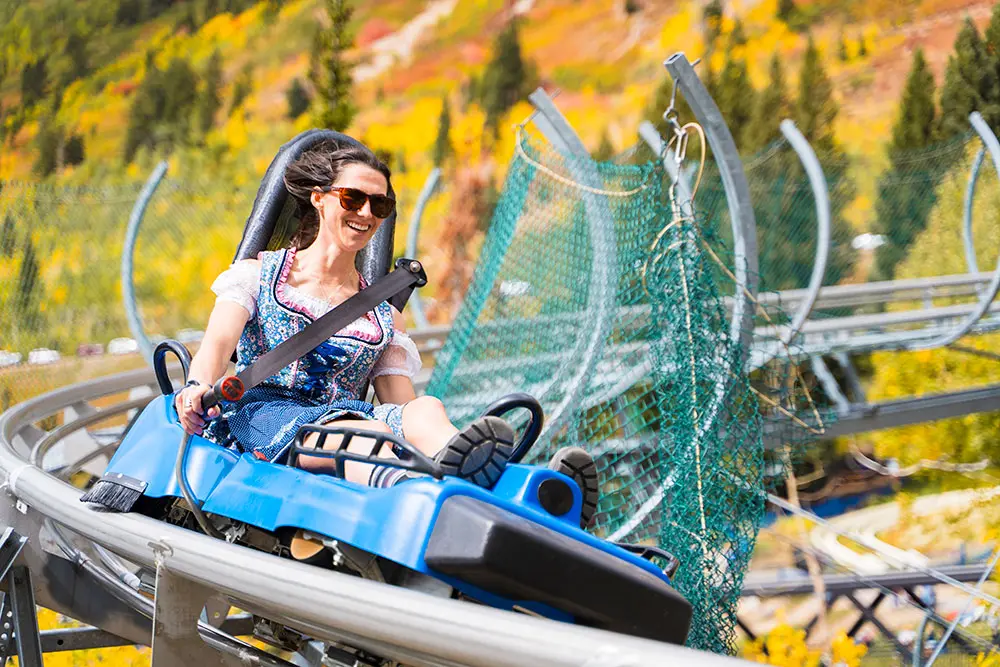 Woman in oktoberfest outfit rides the mountain coaster surrounded by fall colors