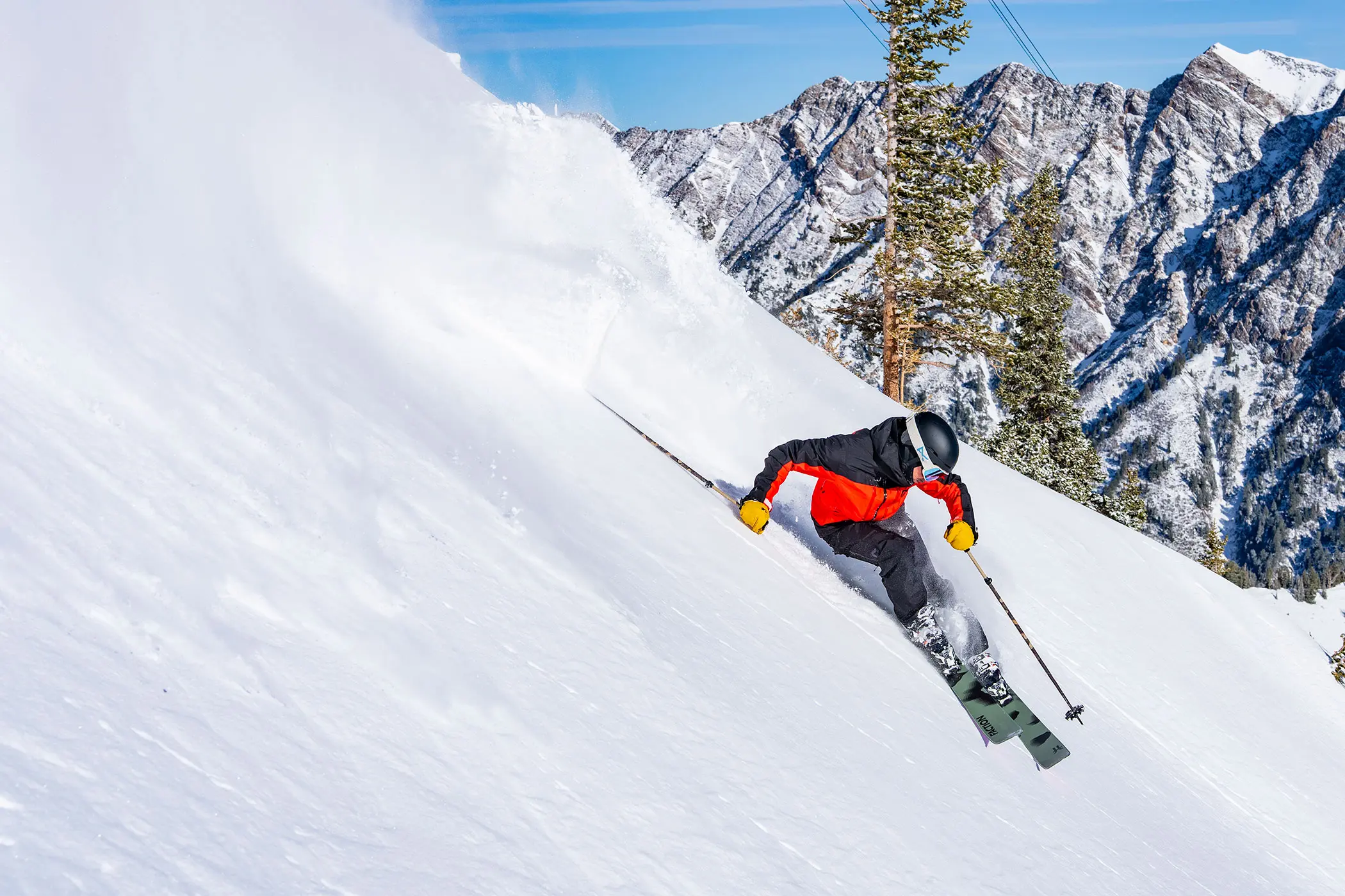 Skier with stay and save discounts skis in powder at Snowbird with a cliff face behind him