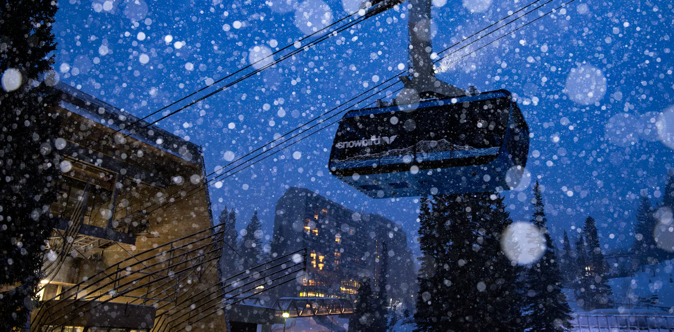Snowbird tram rises above the Cliff Lodge in the dark with snow falling