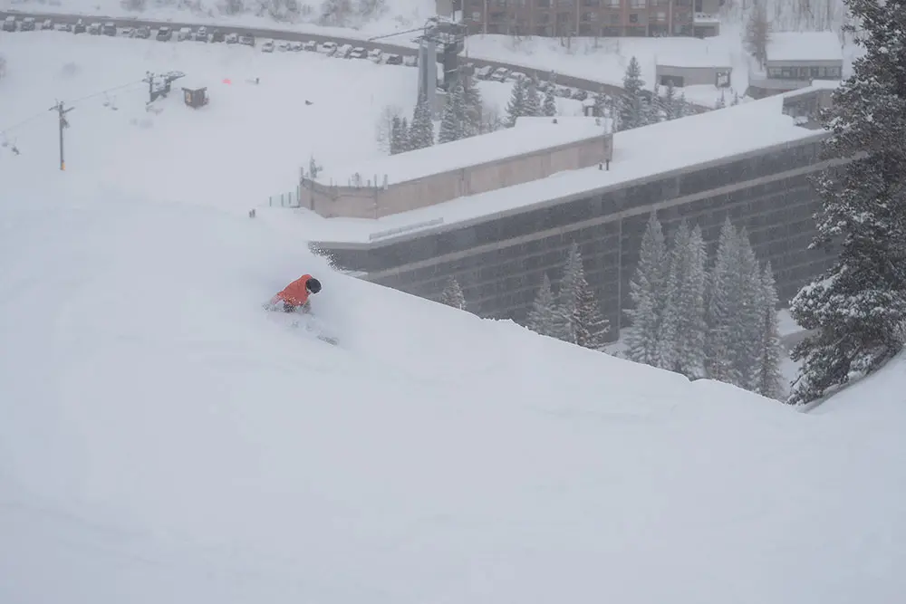 Snowboarder in powder above the Cliff Lodge at Snowbird. Mountain Collective passholder receive exclusive discounts on stays at Snowbird